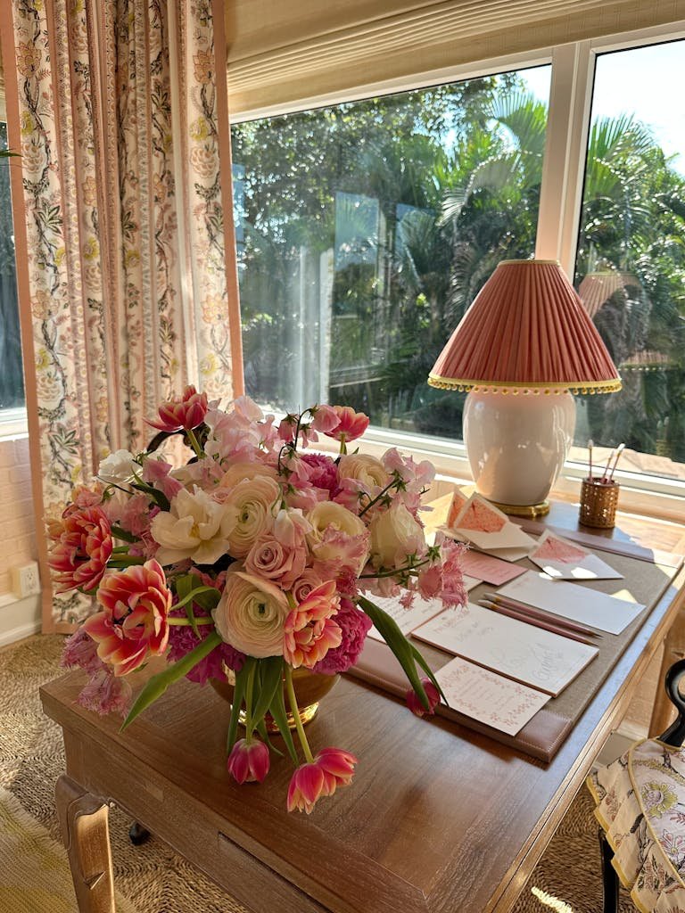 A beautiful floral arrangement on a sunlit desk by a large window, creating a cozy indoor ambiance.