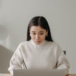 Asian woman in a cozy workspace focused on computer work, showcasing productivity in a modern setting.