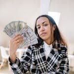 Woman holding American dollars confidently, depicting wealth and success in a bright indoor setting.