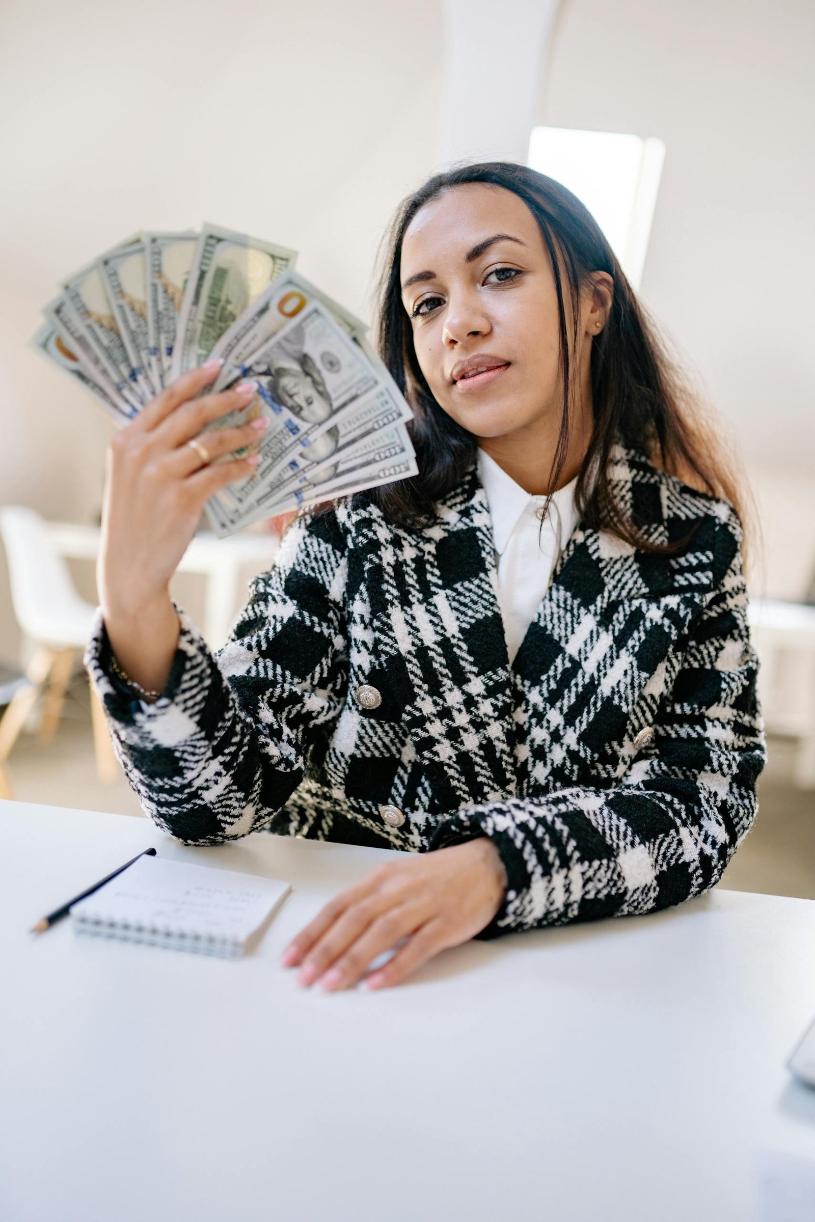 Woman holding American dollars confidently, depicting wealth and success in a bright indoor setting.