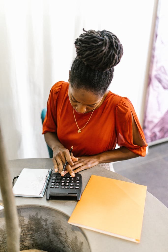 Woman in bright office using a calculator with documents, emphasizing work focus and business tasks.