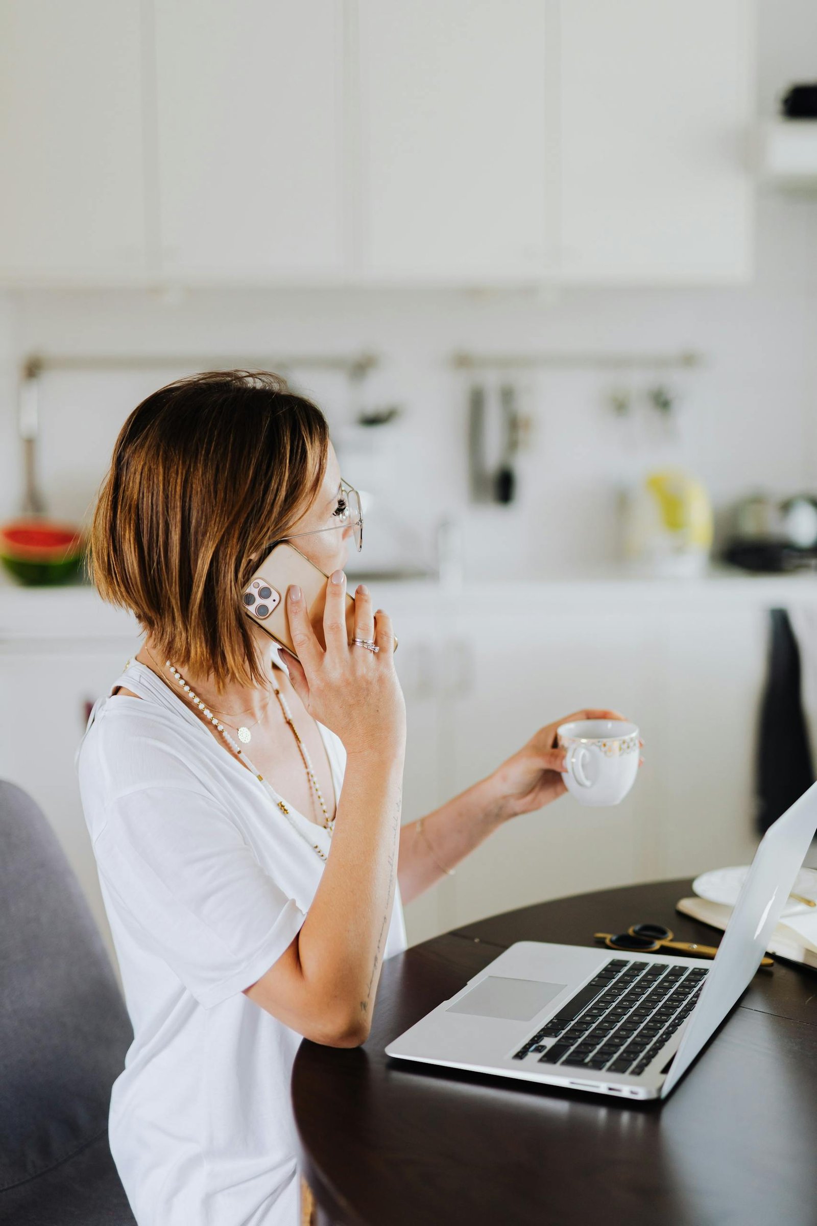 Woman multitasking with a smartphone and laptop while drinking coffee in a cozy home setting working on her budget.