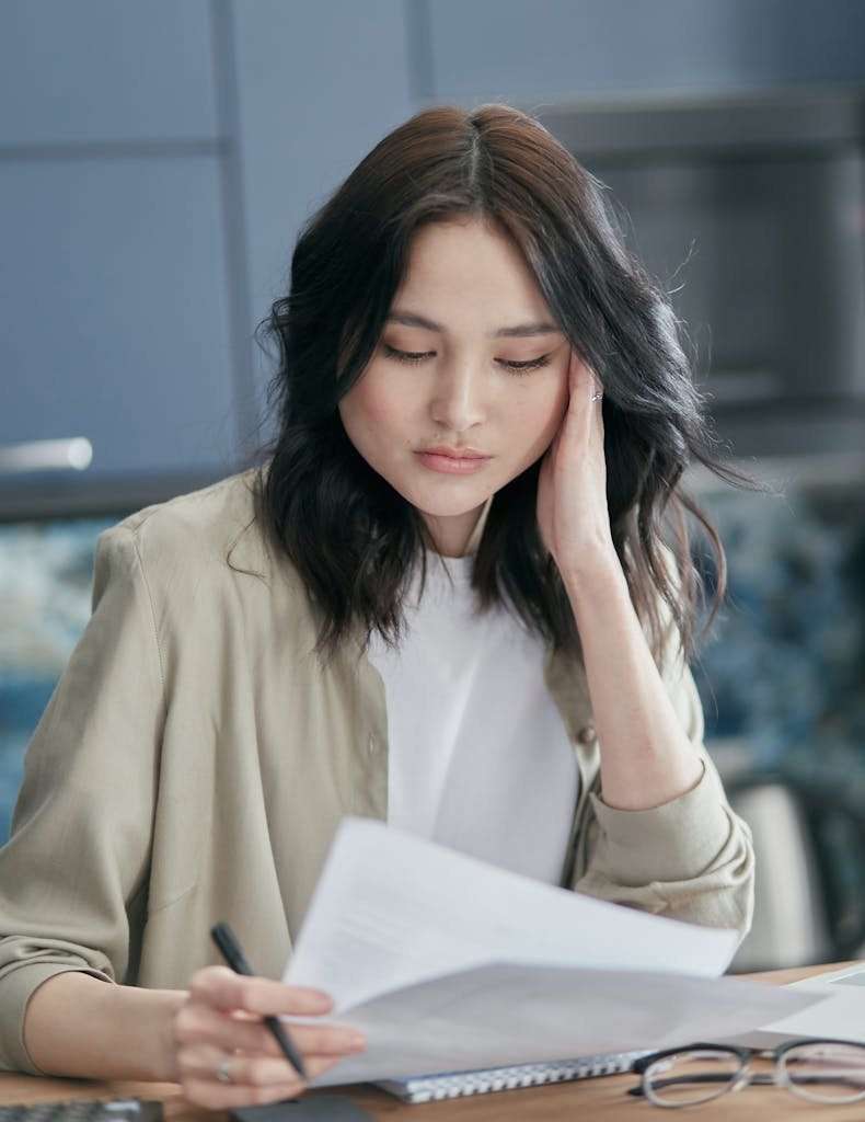 Young woman reviewing paperwork at home, focused and concerned.