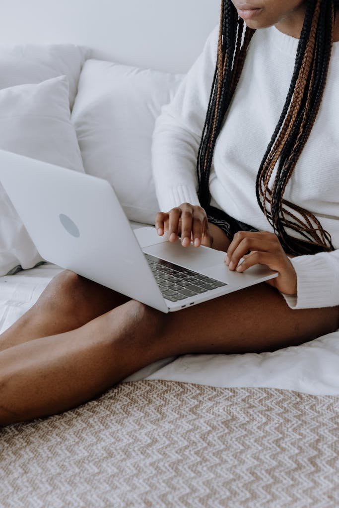 Young woman typing on laptop while sitting on bed in a cozy home setting. Ideal for technology and lifestyle themes.
