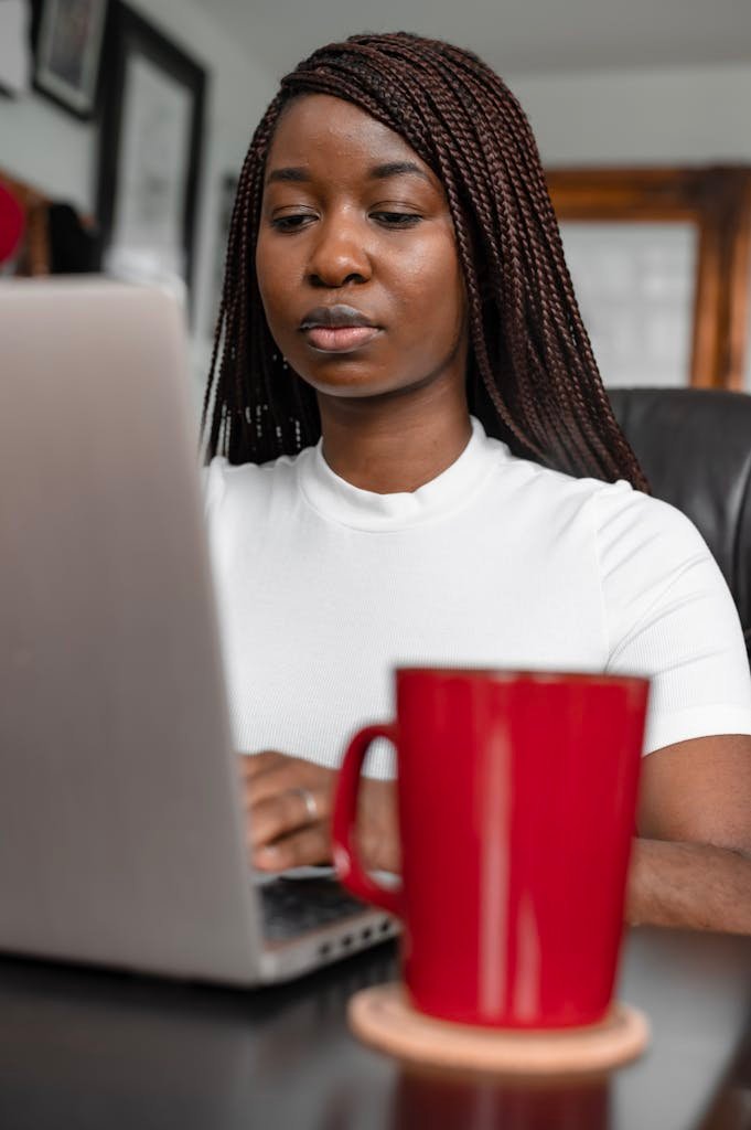 A woman concentrates on her laptop while enjoying coffee at home, embodying remote work lifestyle.