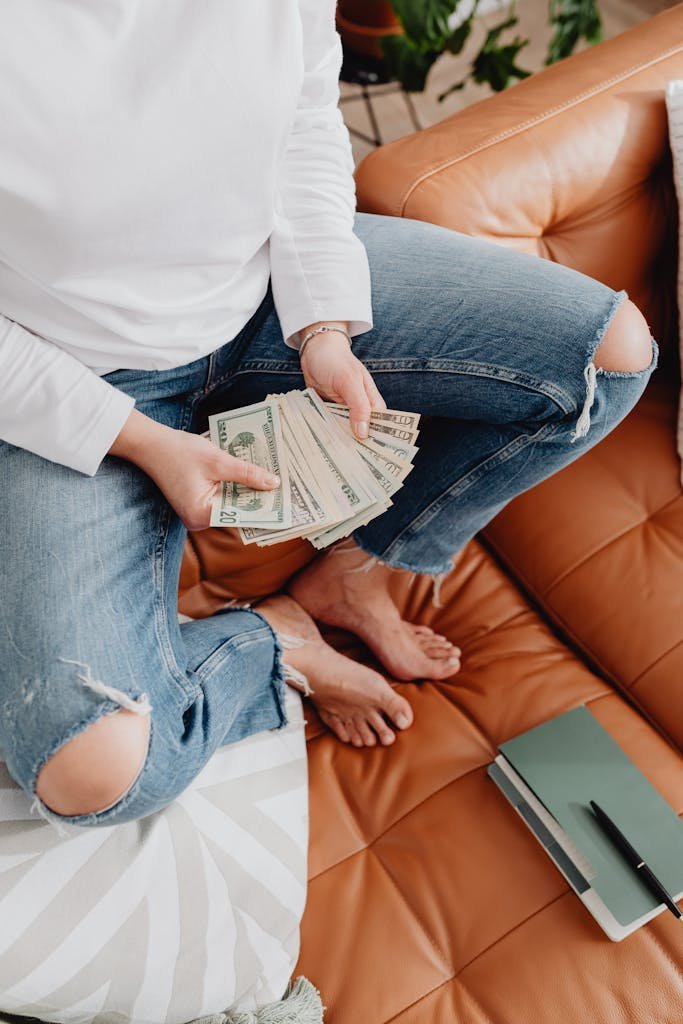 Casual setting with a woman holding dollar bills on a leather sofa, perfect for finance themes.