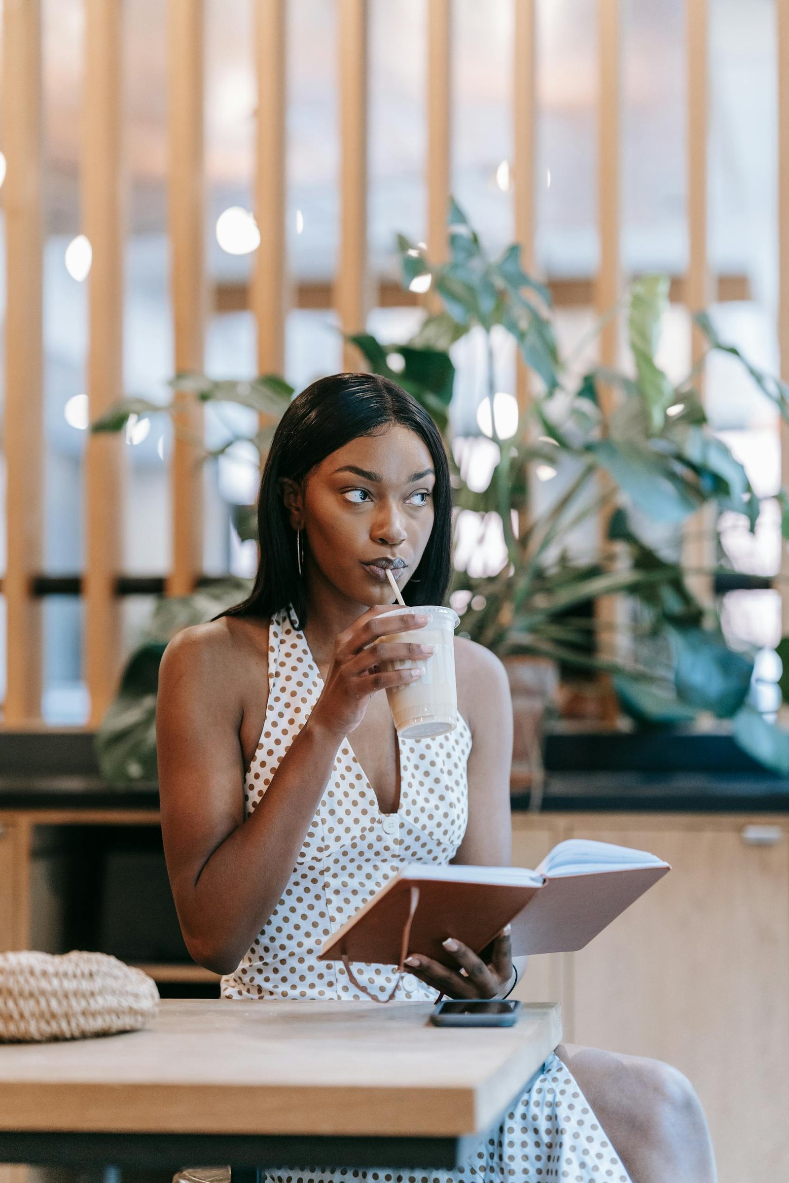 Chic woman in polka dot dress enjoying a drink while writing in notebook.