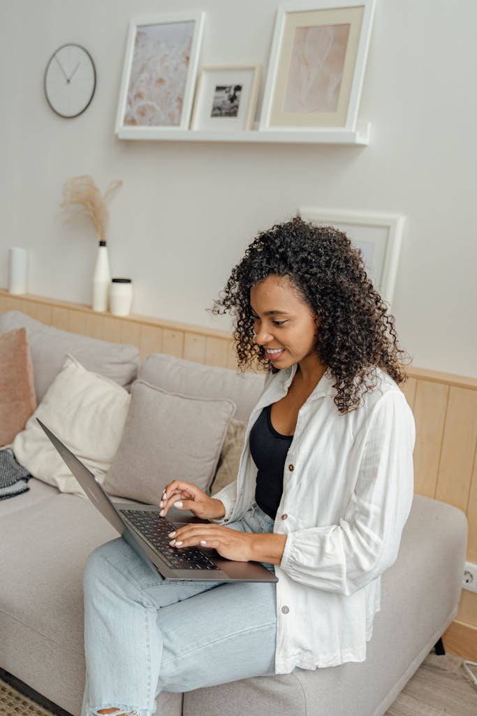 Smiling African American woman working on a laptop at home, sitting comfortably on a sofa.