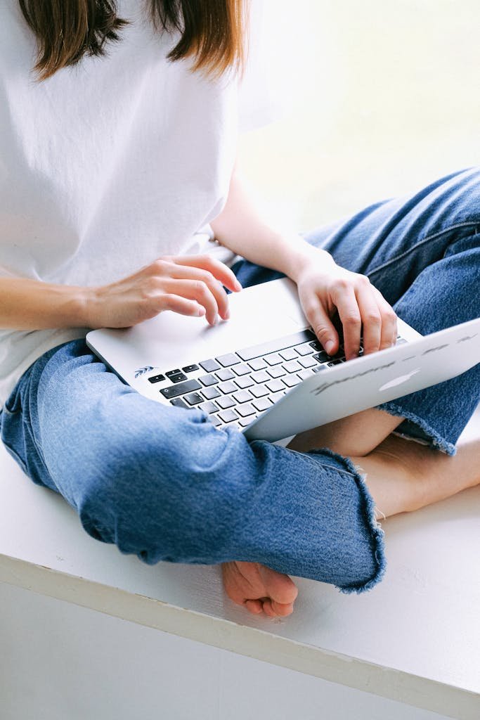 Woman sitting cross-legged in casual jeans working on a laptop indoors. New Year Money System