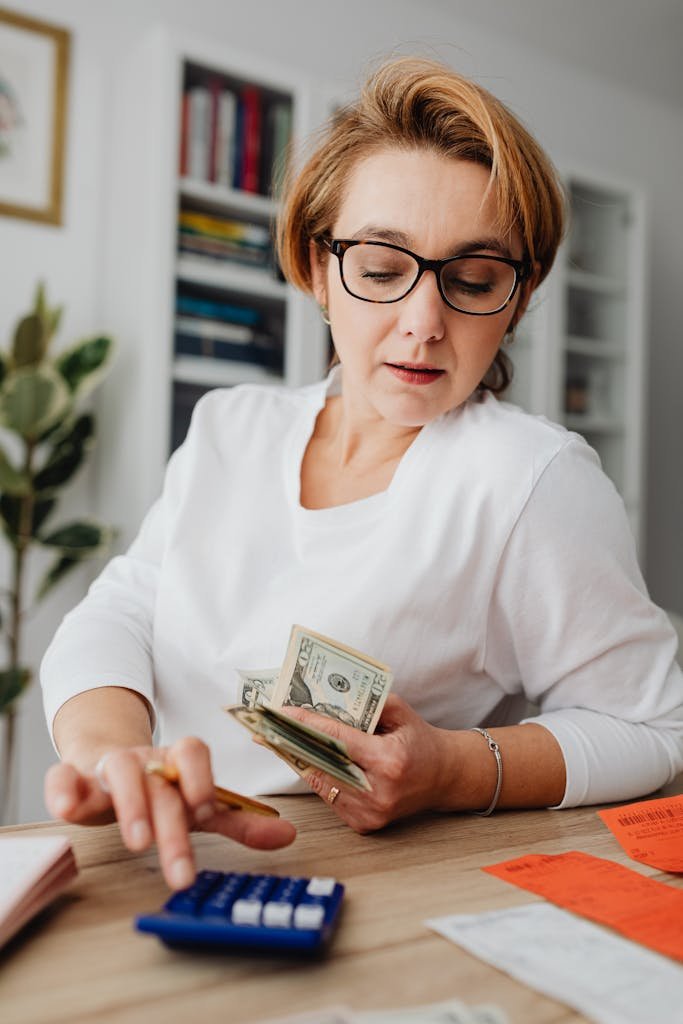 Woman using calculator and handling cash for financial planning at home.