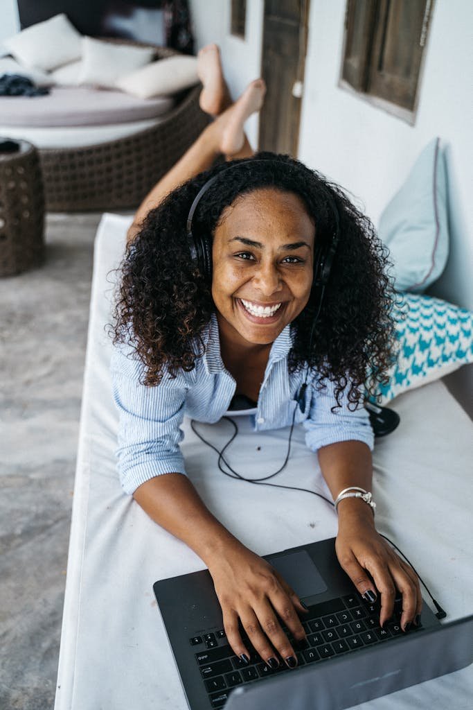 A cheerful woman using a laptop and headset for remote work indoors. Cozy setting, bright mood.