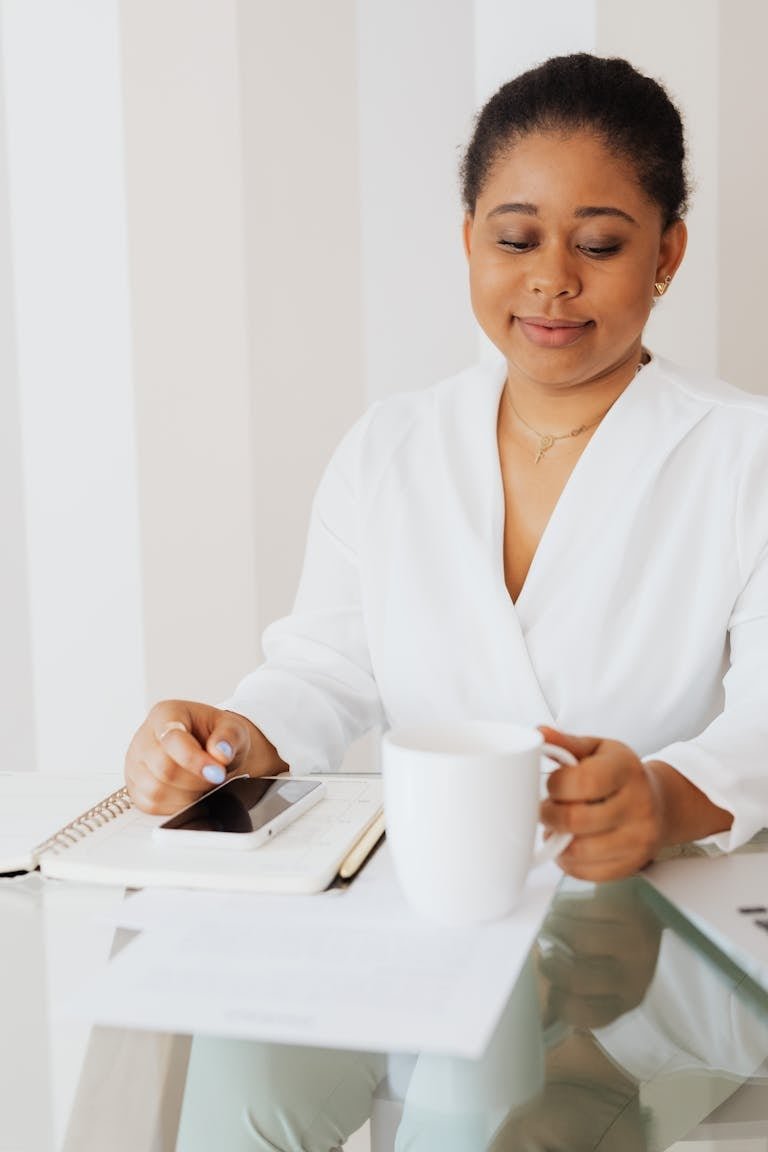 An African American woman enjoys a quiet moment with coffee at a modern office desk.
