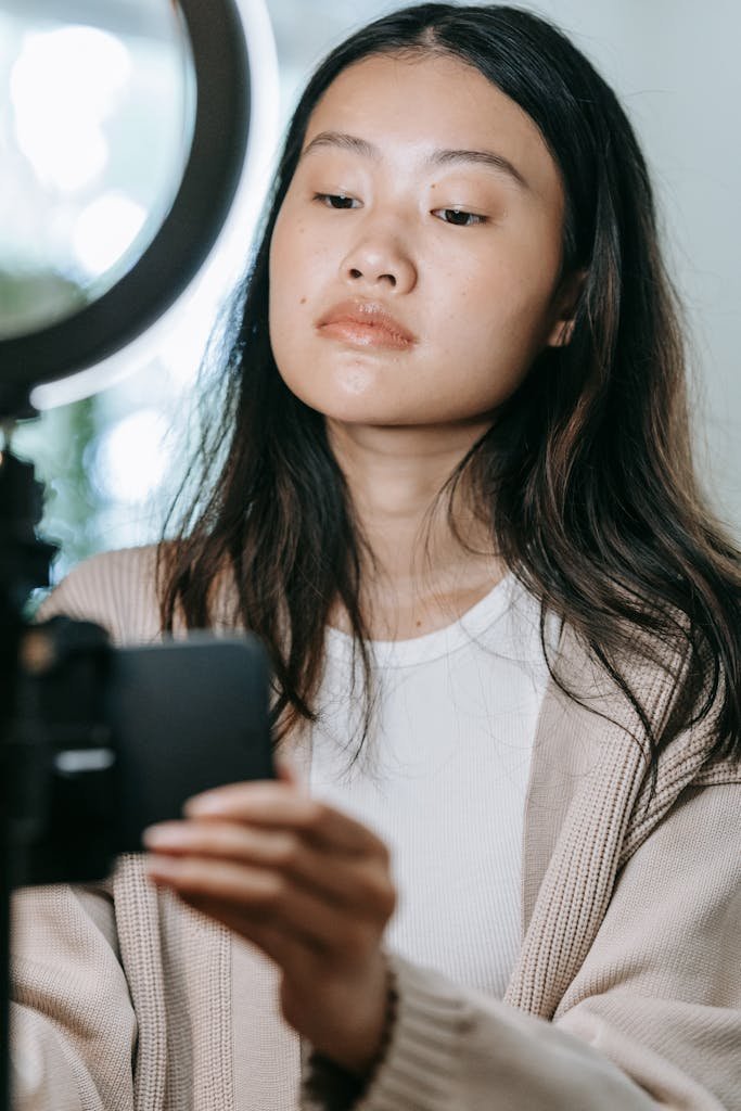 Asian woman using camera and ring light for vlogging indoors.