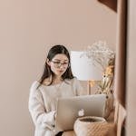 Concentrated young female in trendy casual outfit using laptop while standing near cabinet in cozy living room of modern apartment
