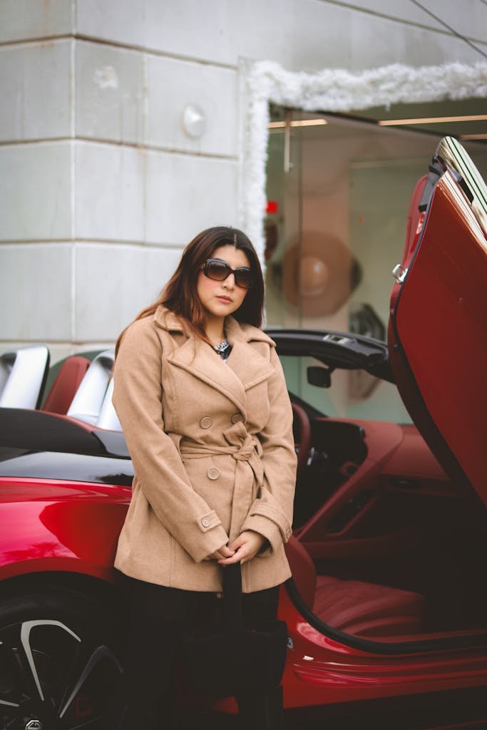 Fashionable woman in sunglasses stands confidently beside a red convertible car. Things I don't spend money on.
