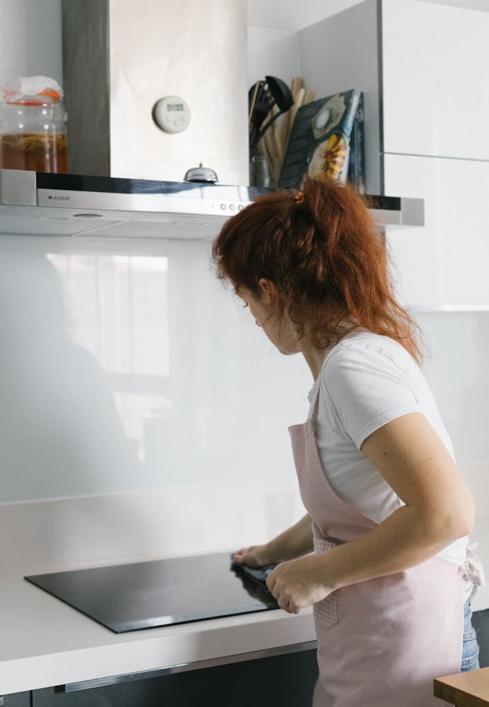 Woman wearing apron cleans kitchen countertop, showcasing a tidy, modern home environment.