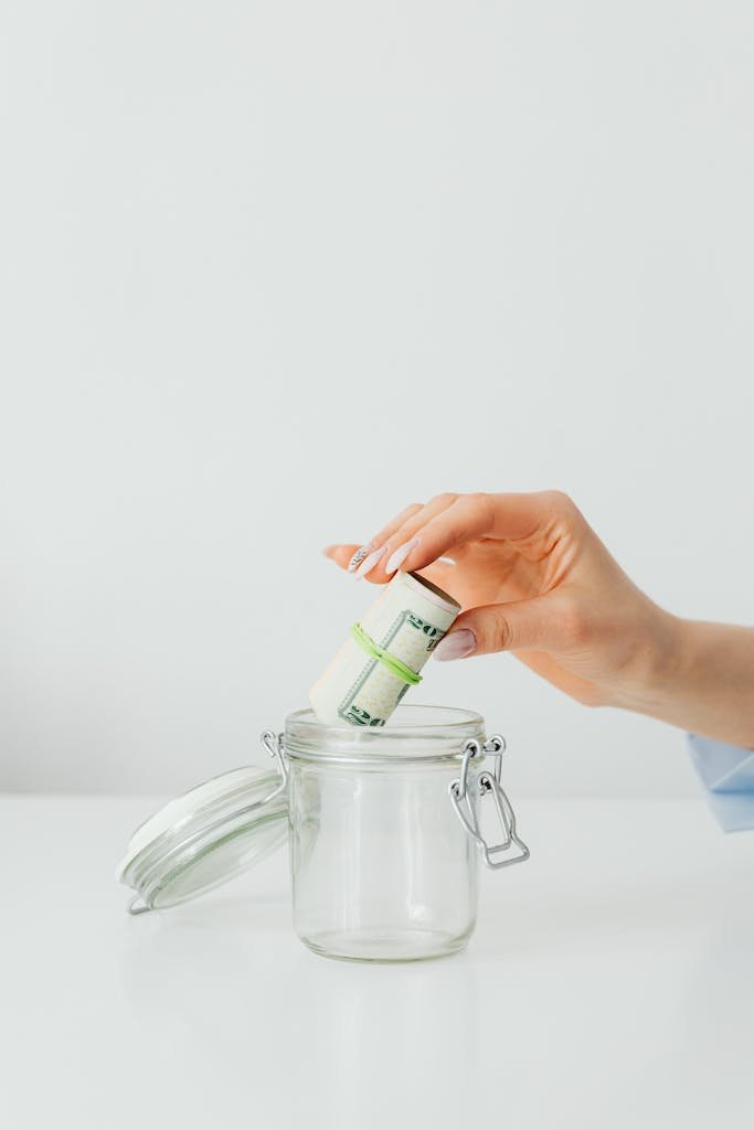A woman placing a rolled stack of banknotes in a glass jar, ideal for finance and savings themes.