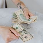 Close-up of hands counting US dollar bills on a marble table, symbolizing personal finance.
