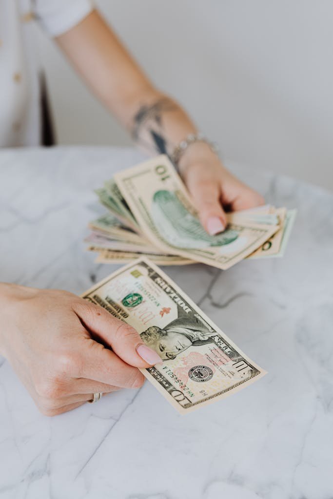 Close-up of hands counting US dollar bills on a marble table, symbolizing personal finance. Cost of living