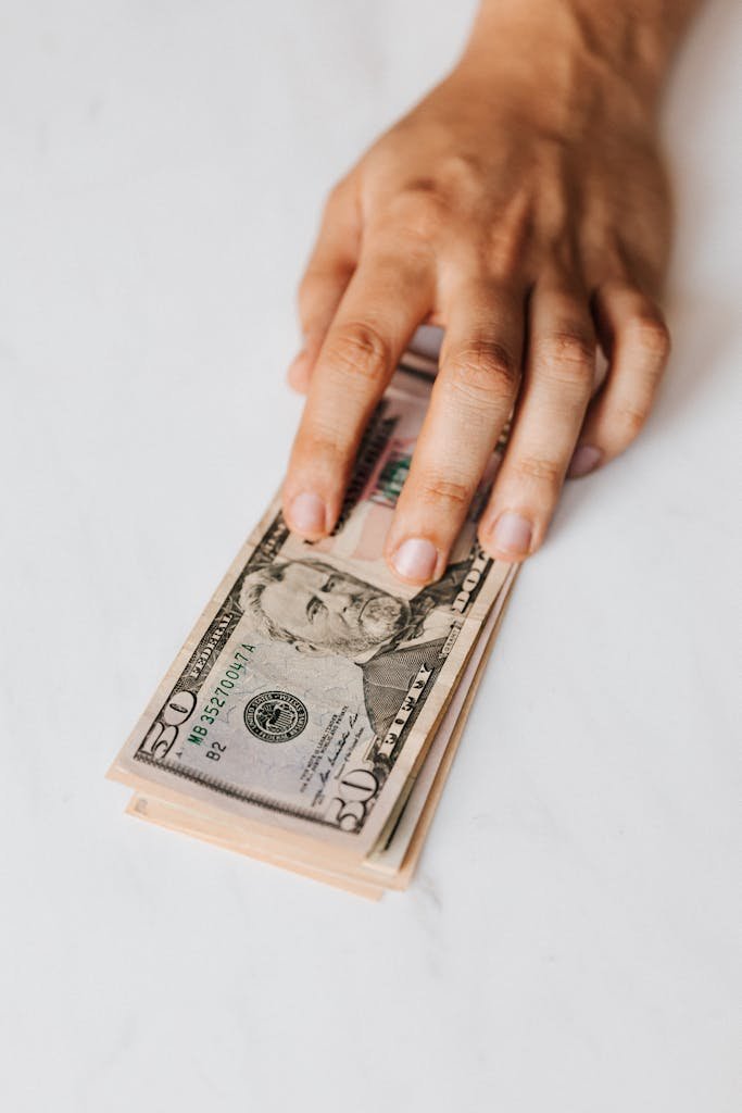 Close-up of a hand holding a stack of fifty-dollar bills on a marble surface, symbolizing finance.