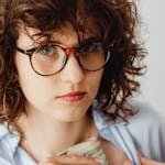 Woman wearing glasses tucks money into her shirt, expressing focus and caution.