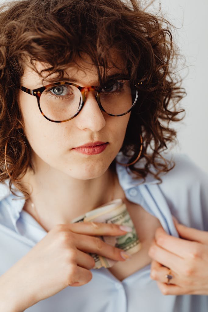 Woman wearing glasses tucks money into her shirt, expressing focus and caution. stability fund