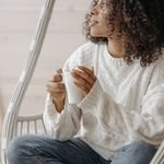 An African American woman with curly hair enjoys coffee in a cozy indoor setting.