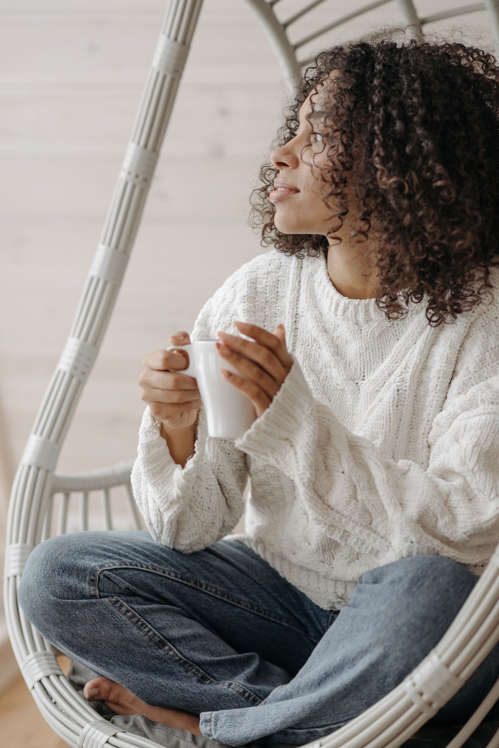 An African American woman with curly hair enjoys coffee in a cozy indoor setting.