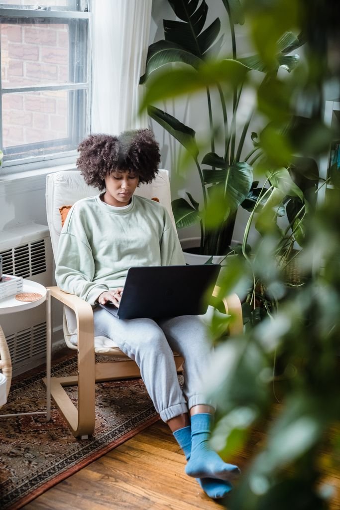 Young woman working on a laptop in a cozy home setting surrounded by plants.